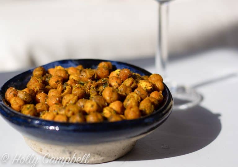 curry roasted chickpeas in a dark blue bowl with a wine glass in the back ground